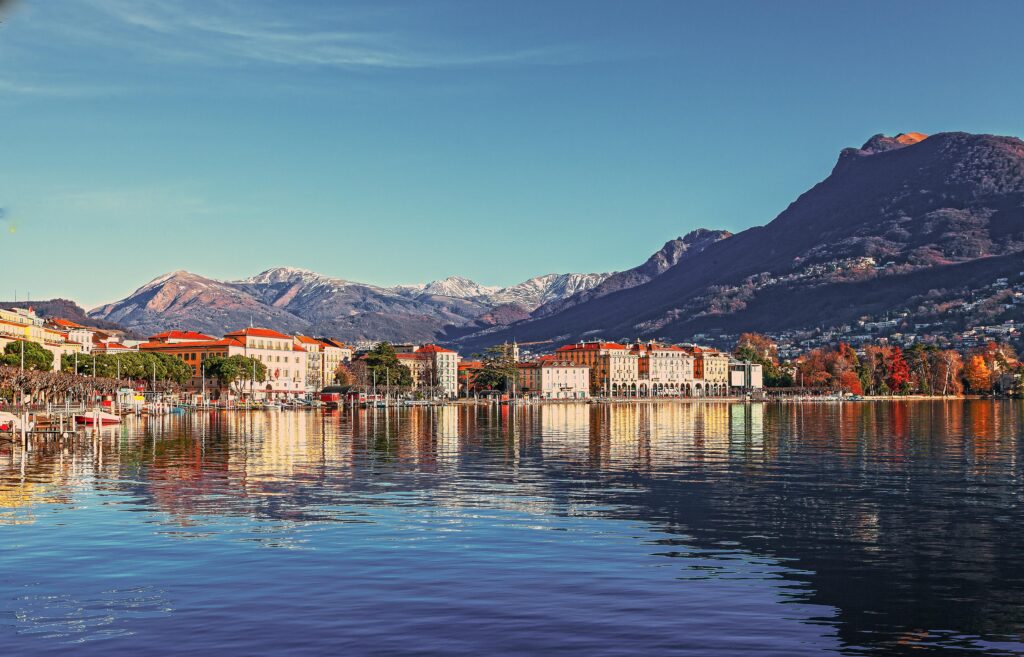 Geneva's lakeside view with colorful buildings and snow-capped mountains in the background, reflecting on the calm waters of Lake Geneva.