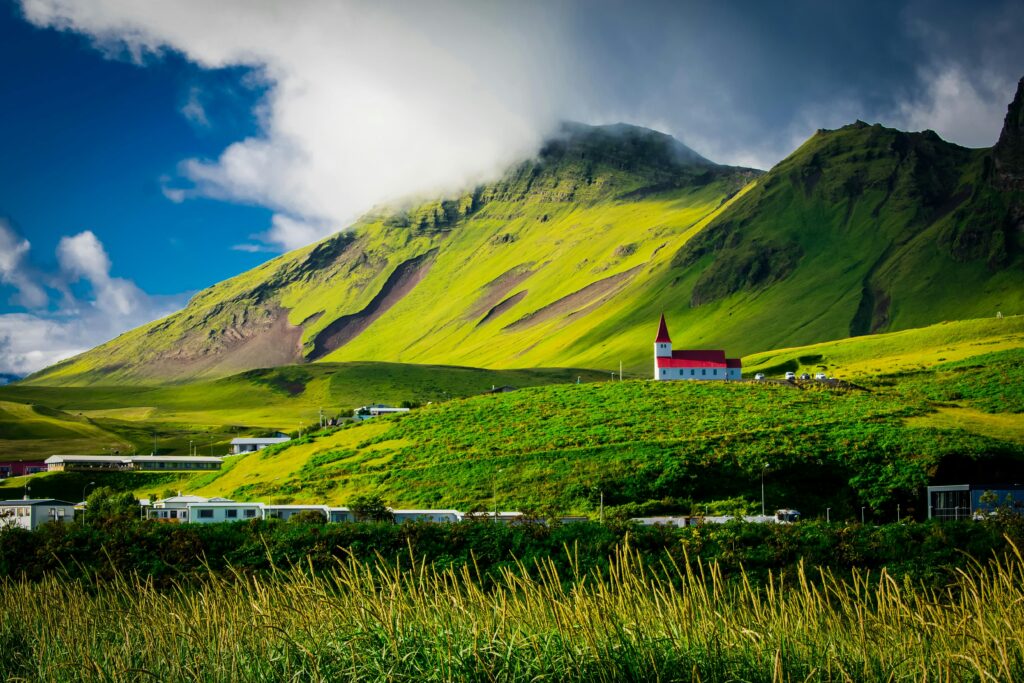 Scenic view of a green valley with a red-roofed church in Iceland, ideal for winter travel destinations with stunning landscapes.