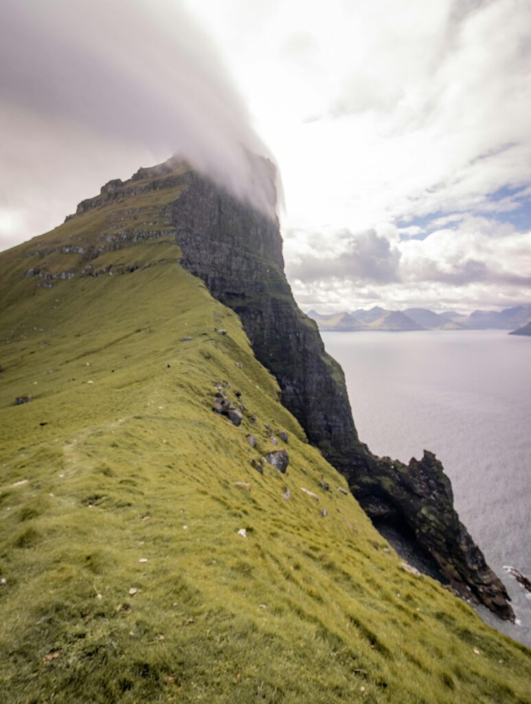 Mist-covered cliff on the Faroe Islands, overlooking the North Atlantic Ocean with dramatic landscapes and lush green terrain.