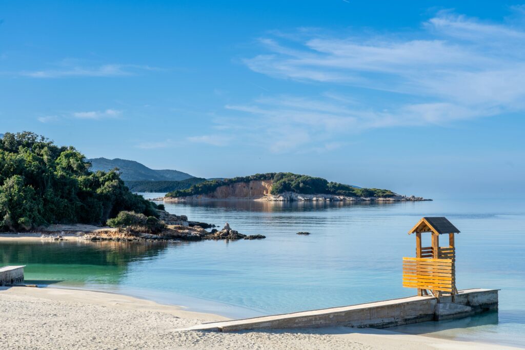 Tranquil view of Ksamil Beach with crystal-clear waters and a small island in the background, a must-visit spot in the Ksamil Travel Guide.