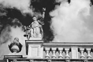 Black and white statue of a historic figure on a classical building with a cloudy sky in Turin, Italy.

